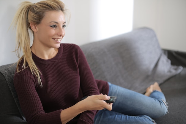 Vista di una bella femmina caucasica seduta sul divano mentre si guarda felicemente la televisione