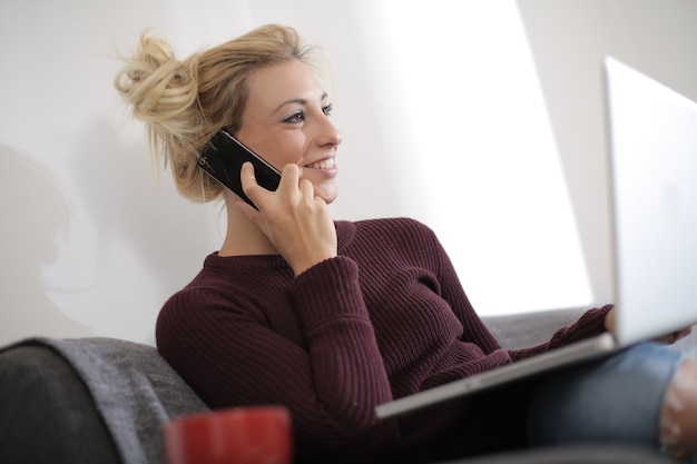 Vista di una bella femmina caucasica seduta sul divano mentre si lavora sul laptop e parlando