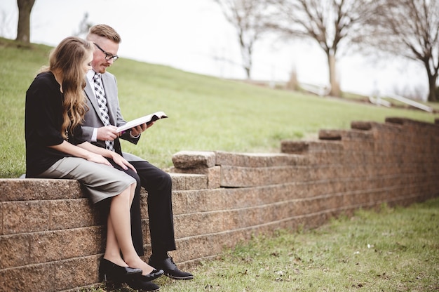 Vista di una coppia che indossa abiti formali durante la lettura di un libro insieme in un giardino