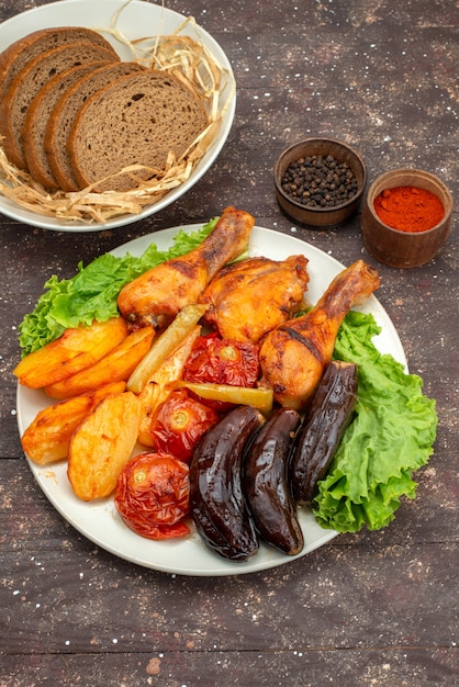 Vista distante superiore cucinato verdure come patate pomodori e melanzane con carne all'interno del piatto bianco con insalata su marrone, pasto di verdure pasto cena