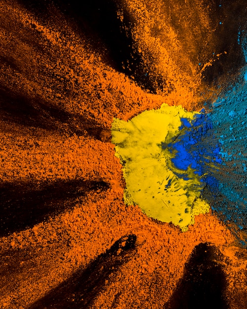 Vista elevata del design giallo, arancione e blu di polvere di holi su sfondo nero