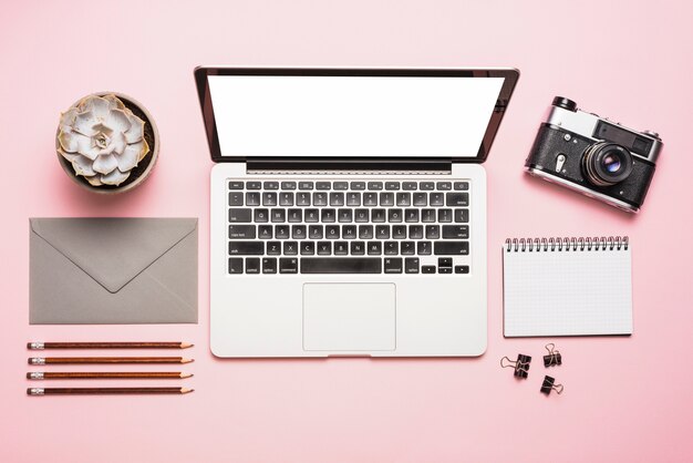 Vista elevata del laptop; telecamera; cartolerie e pianta succulente su sfondo rosa