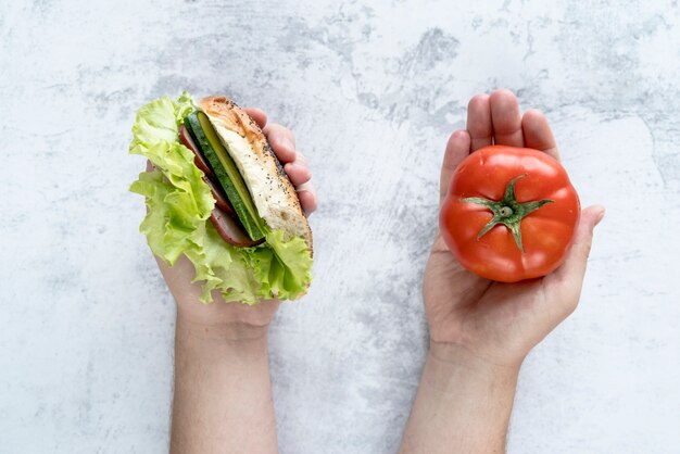 Vista elevata del pomodoro e dell&#39;hamburger della tenuta della mano della persona a disposizione sopra fondo concreto