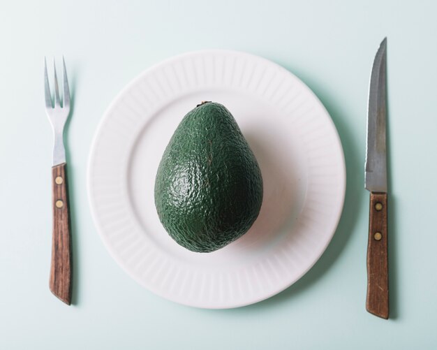 Vista elevata dell&#39;avocado in piatto vicino al coltello e forcella su fondo verde