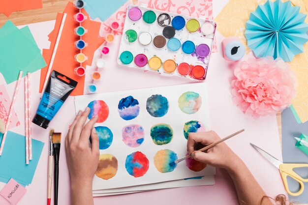 Vista elevata della mano della donna che dipinge cerchio astratto colorato su carta bianca