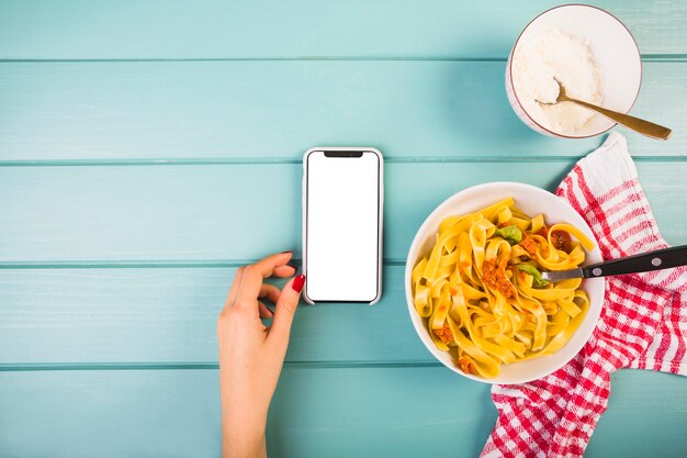 Vista elevata della mano della femmina vicino a smartphone e tagliatelle pasta