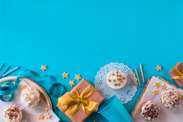 Vista elevata di regali di compleanno con muffin e candele sulla superficie blu