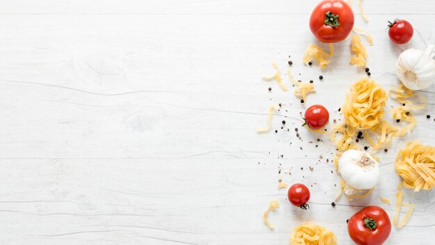 Vista elevata di tagliatelle fresche crude con pomodoro; aglio e pepe nero su tavola bianca