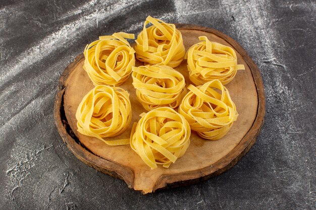 Vista frontale a forma di pasta italiana a forma di fiore crudo e giallo sullo scrittorio di legno marrone