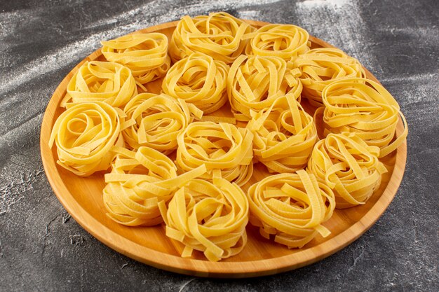 Vista frontale a forma di pasta italiana a forma di fiore crudo e giallo sullo scrittorio di legno