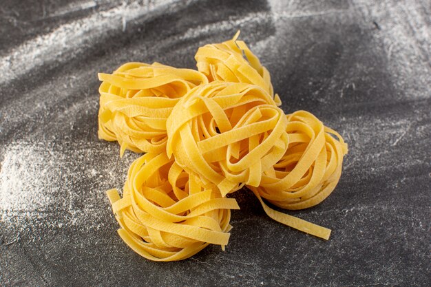 Vista frontale a forma di pasta italiana a forma di fiore grezza e gialla sulla scrivania grigia