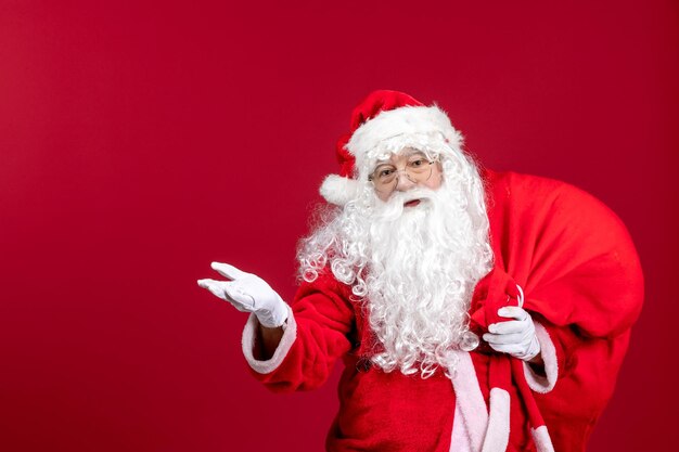 Vista frontale babbo natale che porta una borsa rossa piena di regali durante le vacanze di capodanno con emozione natalizia rossa