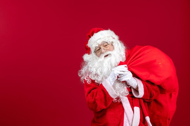 Vista frontale babbo natale che porta una borsa rossa piena di regali durante le vacanze di capodanno con emozione natalizia rossa