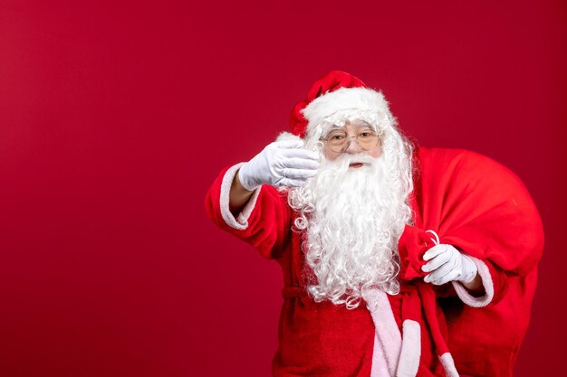 Vista frontale babbo natale che porta una borsa rossa piena di regali sul pavimento rosso emozione capodanno natale