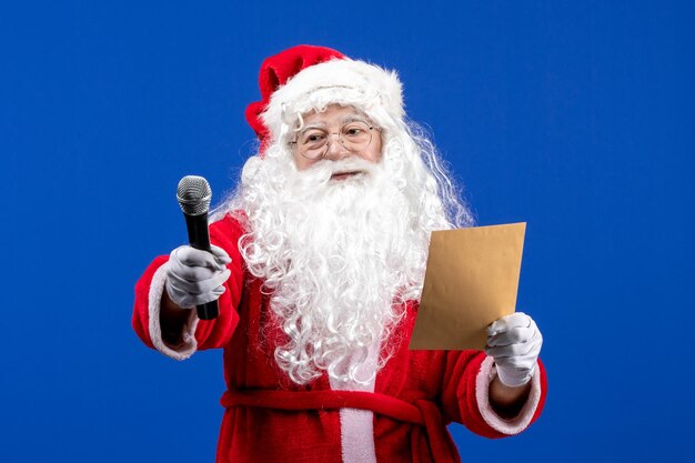 Vista frontale babbo natale che tiene il microfono e legge la lettera sulla neve di natale di colore blu del capodanno