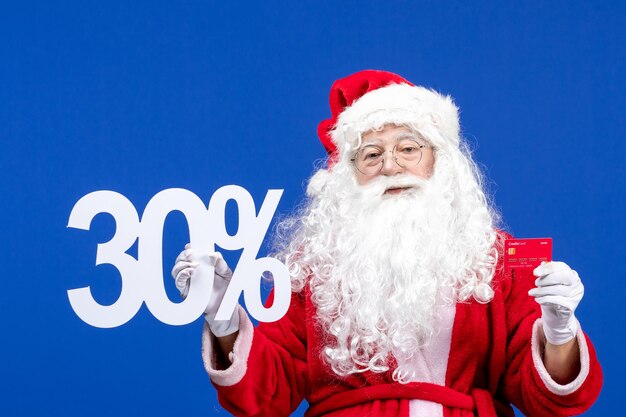 Vista frontale babbo natale che tiene la carta di credito e scrive sul regalo di Natale di colore blu