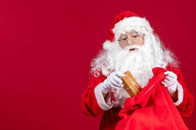 Vista frontale babbo natale che tiene presente dalla borsa piena di regali per i bambini sull'emozione rossa del nuovo anno