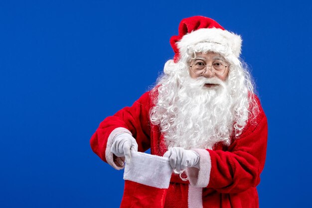 Vista frontale babbo natale che tiene un grande calzino di natale sulla neve di natale di colore blu