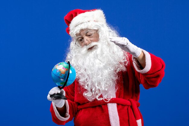 Vista frontale babbo natale che tiene un piccolo globo terrestre sul colore blu del capodanno vacanza natale