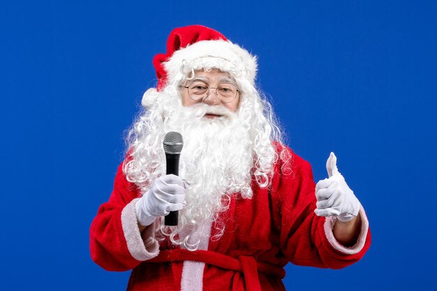 Vista frontale babbo natale con abito rosso e barba bianca che tiene il microfono sul pavimento blu neve vacanze natale colore capodanno