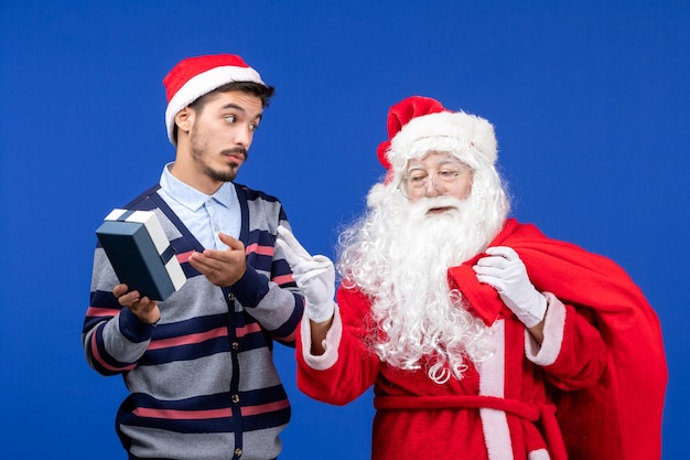 Vista frontale babbo natale con giovane borsa da trasporto maschio piena di regali sul regalo di Natale di colore blu