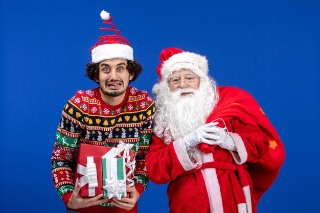 Vista frontale babbo natale con giovane maschio e diversi regali sul colore delle vacanze di natale emozione blu