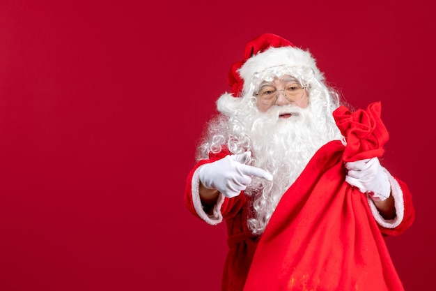 Vista frontale babbo natale con la borsa rossa piena di regali sul colore rosso dell'emozione di natale delle vacanze di capodanno