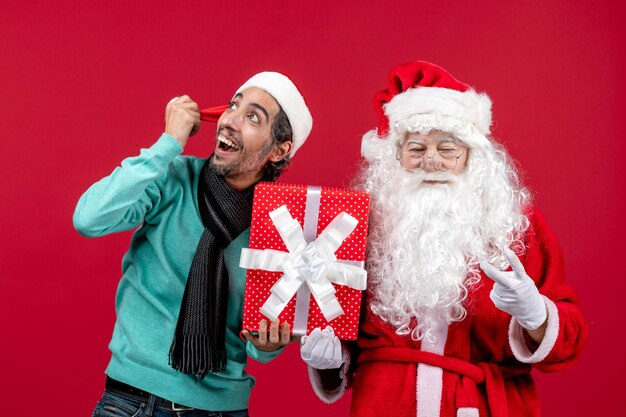 Vista frontale babbo natale con maschio che tiene regalo di festa sul pavimento rosso regalo emozione rosso natale