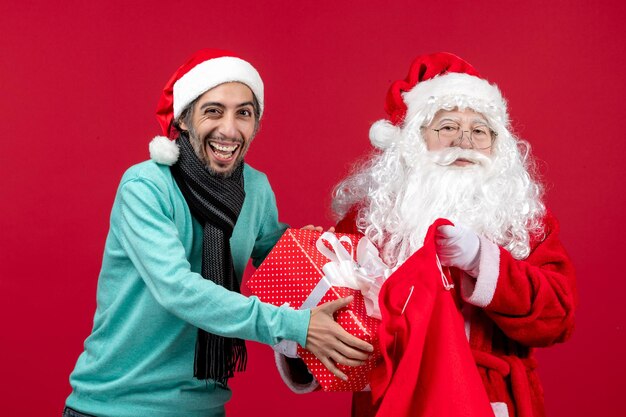 Vista frontale babbo natale con maschio che tira fuori il regalo dalla borsa sul colore rosso delle vacanze di emozioni di natale