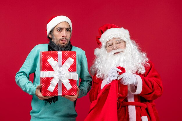 Vista frontale babbo natale con maschio che tira fuori il regalo dalla borsa sulla scrivania rossa natale emozione colore rosso