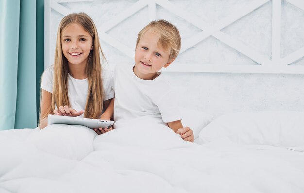 Vista frontale bambini che soggiornano nel letto mentre giocano su un tablet