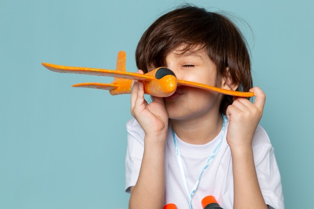 vista frontale bambino ragazzo carino adorabile giocare con l'aereo giocattolo arancione sulla scrivania blu