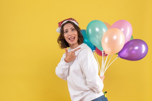 Vista frontale bella femmina nascondendo palloncini colorati su giallo