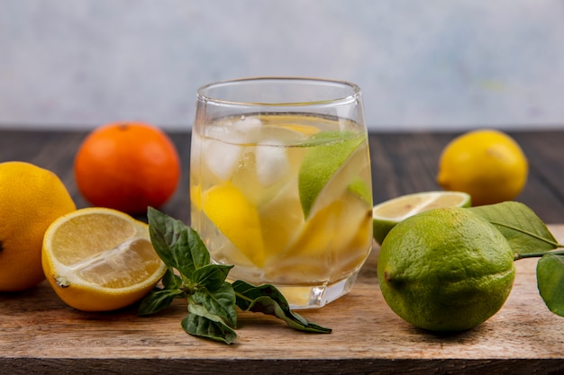 Vista frontale bicchiere d'acqua con menta, limone e spicchi di lime su un tagliere