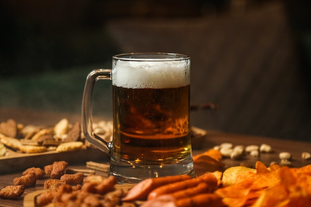Vista frontale bicchiere di birra con birra snack crostini patatine e salsiccia sul tavolo