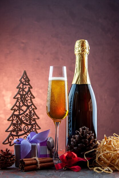 Vista frontale bicchiere di champagne con regali e bottiglia su bevanda leggera alcol foto colore champagne capodanno