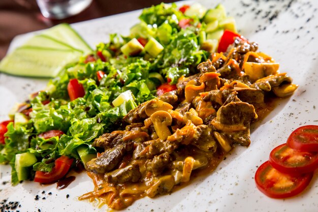 Vista frontale carne fritta con funghi in salsa con insalata di verdure e fette di pomodoro e cetriolo