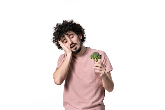 Vista frontale che dorme giovane maschio che tiene piccoli broccoli verdi su bianco