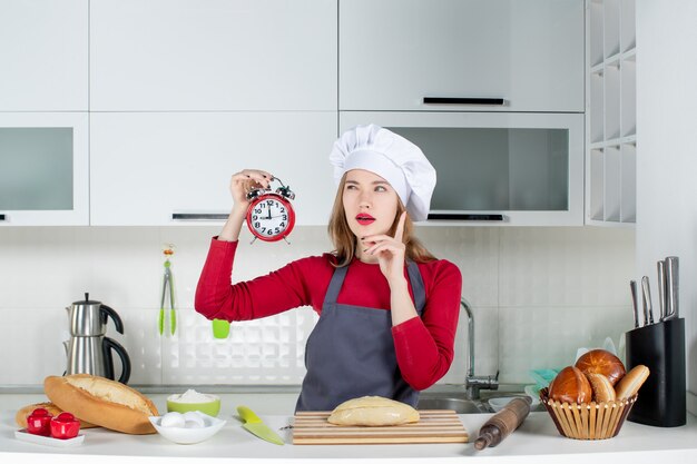 Vista frontale che pensa giovane donna con sveglia rossa in cucina