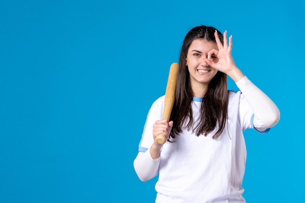 Vista frontale che posa giovane femmina con la mazza da baseball sull'azzurro