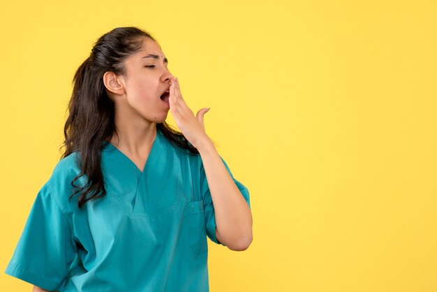 Vista frontale che sbadiglia medico femminile in uniforme in piedi su sfondo giallo