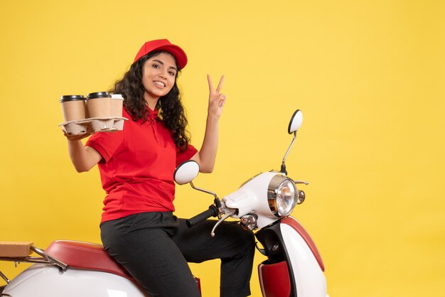 Vista frontale corriere femminile in bici per la consegna del caffè sullo sfondo giallo lavoro di servizio uniforme lavoratore donna consegna lavoro