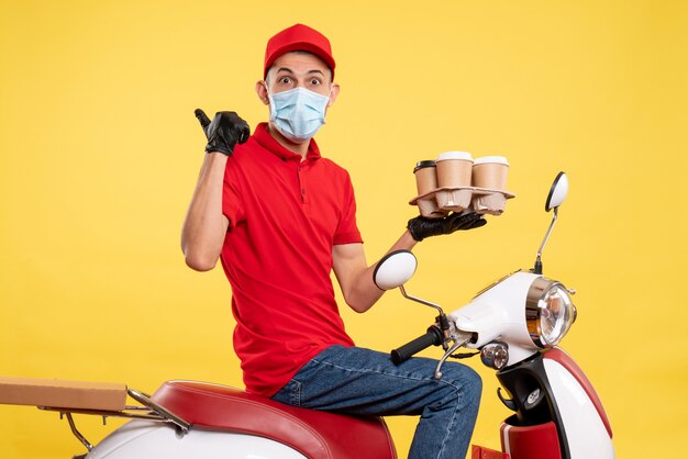 Vista frontale corriere maschio in uniforme rossa e maschera con caffè sul colore giallo lavoro pandemia consegna covid- lavoro servizio di ristorazione