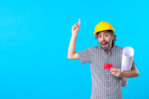 Vista frontale costruttore maschio che tiene piano e carta di credito su sfondo blu denaro design edificio lavoro casco lavoro architettura a colori
