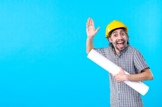 Vista frontale costruttore maschio in casco giallo con piano su sfondo blu lavoratore proprietà architettura costruttore costruzione lavoro ingegneri