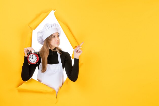 Vista frontale cuoca in berretto bianco da cuoco con orologio su foto gialla lavoro a colori emozione cucina cucina cibo solare