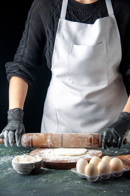 Vista frontale cuoca stendere la pasta con la farina su una torta scura lavoro forno hotcake cuocere lavoratore uovo cucina pasta