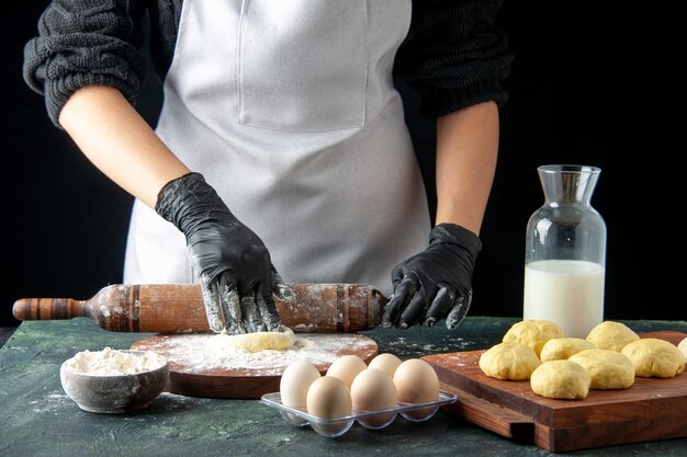 Vista frontale cuoca stendere la pasta con la farina sulla torta scura lavoro forno impasto hotcake cuocere torta lavoratore cucina a base di uova