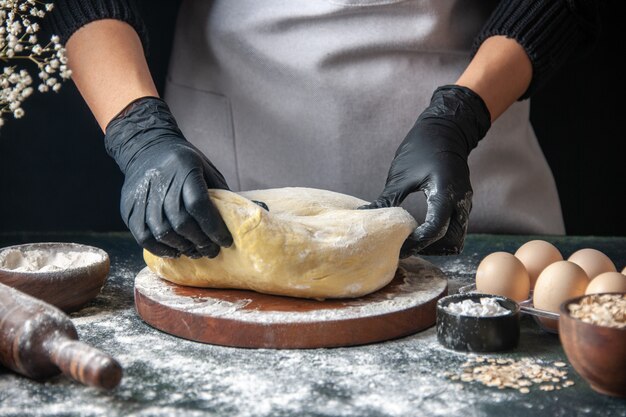 Vista frontale cuoca stendere la pasta sul lavoro di pasticceria scura pasta cruda hotcake forno a torta forno