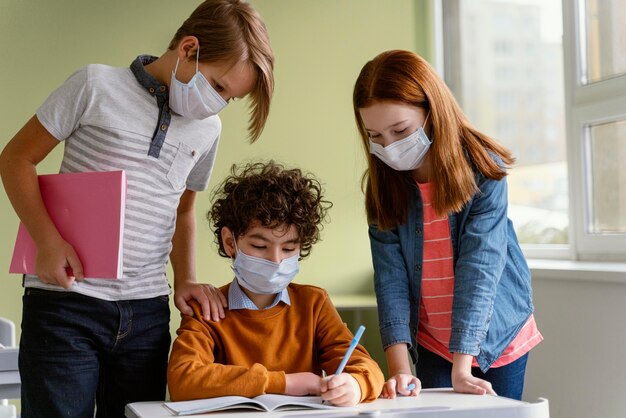 Vista frontale dei bambini con maschere mediche che imparano a scuola